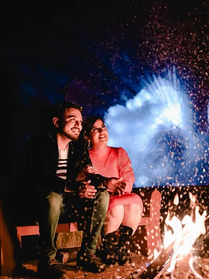 Another perspective of the bonfire scene, capturing the couple's happy expressions as they enjoy the moment. The sparks create a magical, celebratory feel for this anniversary or pre-wedding photo.