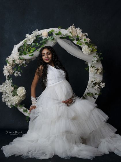 An angelic portrait in white. The floral hoop and dark background make the white ruffled gown stand out beautifully.