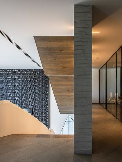 This office interior features bold edges and clean lines, with a staircase that speaks volumes. The design, for a financial advisor, uses geometric forms and a textured feature wall to symbolize the energy and fluctuations of the market.