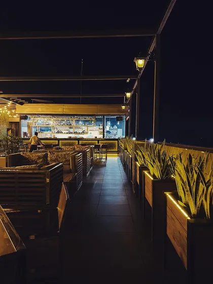 A long view of the rooftop cafe layout, showing the arrangement of seating along the perimeter. We used a line of tall planters to create a natural boundary and enhance privacy, with strategic lighting to guide the eye and define the space.