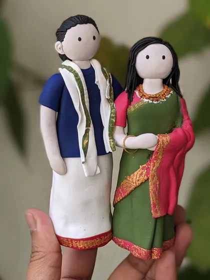 A closer look at the custom couple figurine, showcasing the detailed clothing. The woman is in a green and pink saree with gold accents, and the man is in a traditional dhoti. I take care to replicate the attire from your photos.