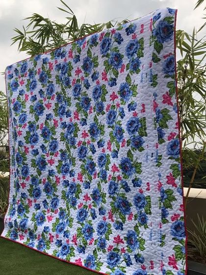 A beautiful floral quilt with blue roses, displayed outdoors.