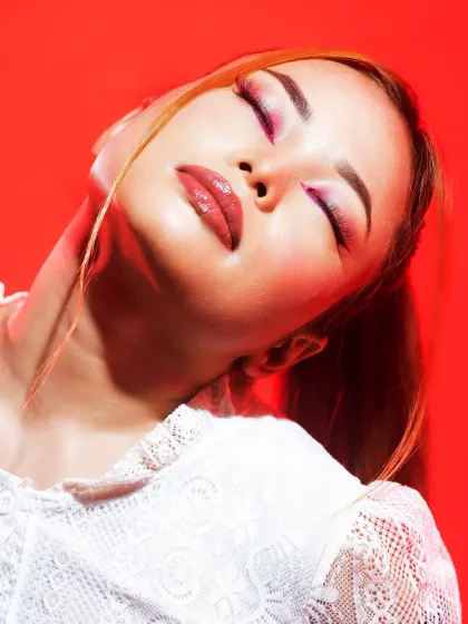 A dreamy, high-fashion look with a wash of pink on the eyes and glossy lips, set against a vibrant red background for maximum impact.