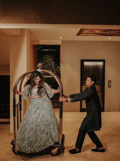 A fun and spontaneous moment inside a hotel. The groom playfully pushes his laughing bride on a luggage cart, showing that great photos can happen anywhere.