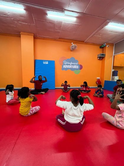 A class of young children and their instructor sit in a circle, flexing their muscles. This opening circle activity helps kids focus, follow instructions, and feel like part of a team.