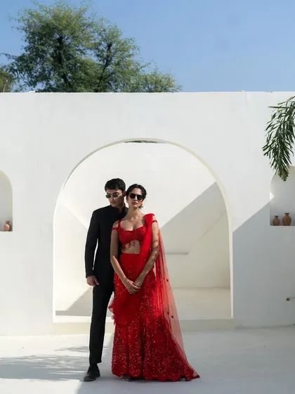 We provide value-for-money service with on-trend pieces. This couple looks stunning in a red sequin saree and a classic black bandhgala suit.