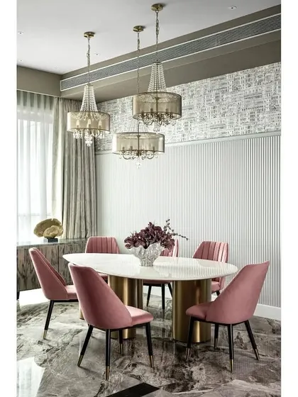 A six-seater dining table with an unconventional teardrop shape and off-center chandeliers. The fluted wall paneling continues from the living area, visually elongating the space and connecting the dining and lounging zones.