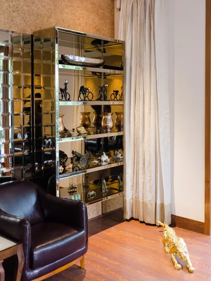 Every corner is an opportunity for personal expression. This nook combines a classic leather armchair with a mirrored cabinet displaying personal artifacts, reflecting the family's history and taste within the modern architectural frame.