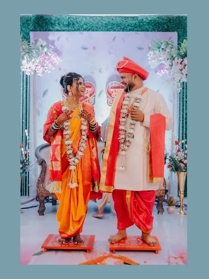 A full-length portrait of the couple during their 'Jaimala' ceremony, standing on small stools as is traditional.