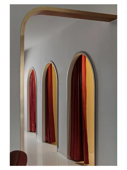 A hallway of arched doorways with dramatic red curtains creates a theatrical and rhythmic procession. This design element provides privacy for treatment rooms while adding a bold, repeating visual motif that is central to the salon's identity.