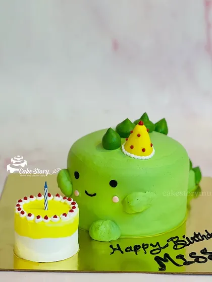 An adorable dinosaur-shaped cake for a birthday celebration. This cute green dino comes with its own mini birthday cake, making it a fun and unique design.