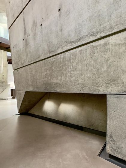 A low-level opening in a concrete wall of the 'House of Stories'. These small, considered apertures are designed to bring in focused pools of light, adding another layer of texture and mystery to the interior spaces.