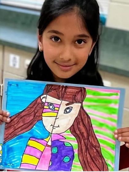 This student proudly displays her creative split-face portrait, a project that challenges older students to think about identity and artistic style.