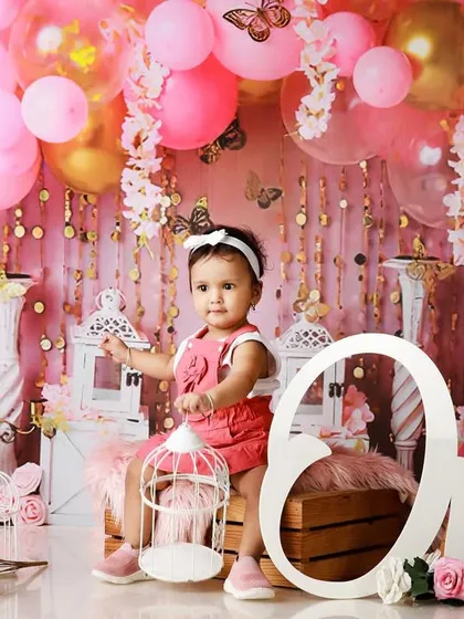 A pink and gold-themed first birthday shoot, with the baby girl sitting happily among balloons and lanterns.