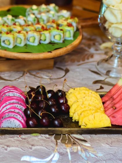 A beautiful spread showing sushi rolls on a banana leaf alongside a platter of exotic fruits like dragon fruit, cherries, and pineapple.