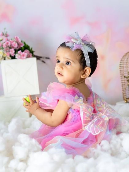 A dreamy portrait of a little fairy sitting among the clouds. The soft pinks, florals, and ethereal setting make for a truly magical and whimsical photograph.