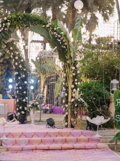 A charming and rustic wedding entrance arch made with banana leaves and white flowers. The hand-painted welcome sign adds a personal and whimsical touch to the ceremony decor.
