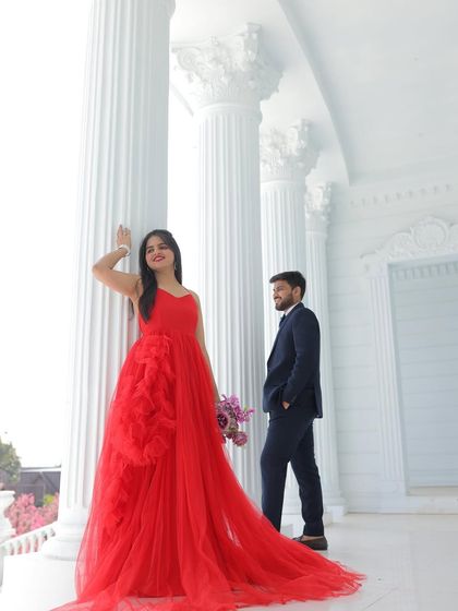 A stylish and modern pre-wedding portrait. The red ruffled gown looks chic and sophisticated against the clean lines of the white pillars.