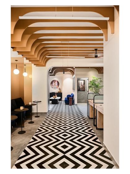 The central corridor features a striking black and white tiled floor that resembles a carpet, leading the eye through the space. The arched ceiling fins and informal seating nooks create a warm and inviting pathway.