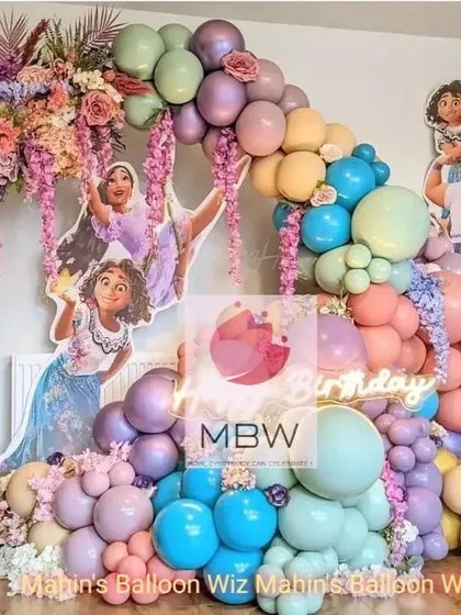 A magical Encanto-themed birthday party. The decor features characters from the movie, a cascade of colorful flowers, and a beautiful pastel balloon arch, capturing the spirit of the film.