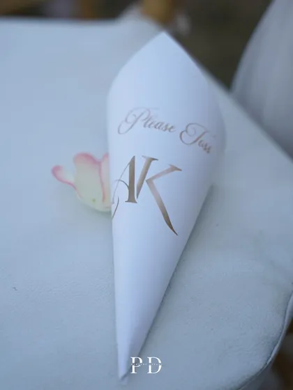 A personalized paper cone for the petal toss, featuring the couple's initials. A small, thoughtful detail that enhances the guest experience.