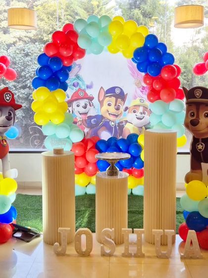 A bright and cheerful Paw Patrol birthday setup with a rainbow-colored balloon arch and character standees.
