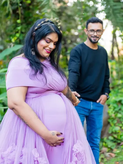 A candid shot of the couple walking hand-in-hand. The focus is on the mom-to-be and her beautiful baby bump, dressed in a lovely lavender gown.