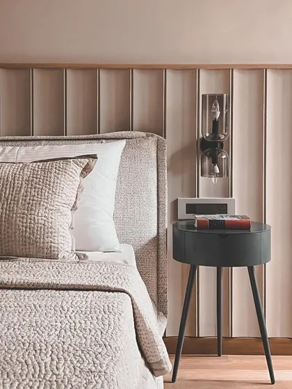 This bedroom detail shows a fluted wall panel behind the bed, adding texture and depth. The minimalist side table and modern wall sconce complete the clean, sophisticated look.