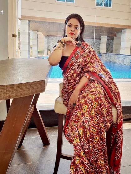 A vibrant red patola print saree paired with a simple black blouse, styled for a chic, modern look by the poolside. This demonstrates the versatility of traditional fabrics.