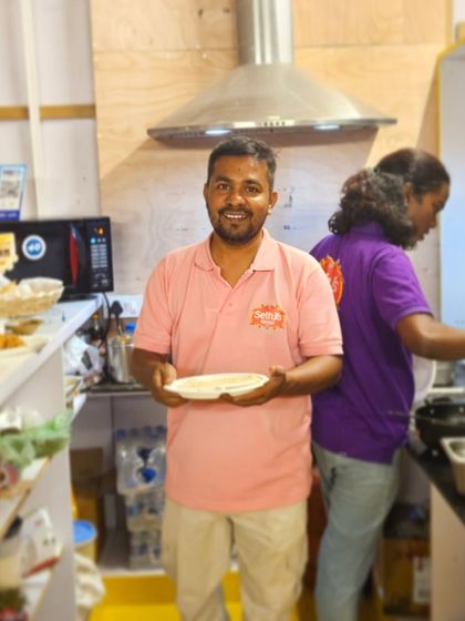 Deepak in the kitchen, holding a plate and smiling. Behind him, you can see the hustle and bustle of our food preparation.