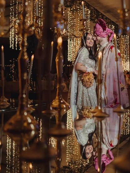 A creative shot of the couple reflected in a mirrored floor, surrounded by hundreds of candles and hanging lights. This setup creates an illusion of infinite light and romance for a reception.