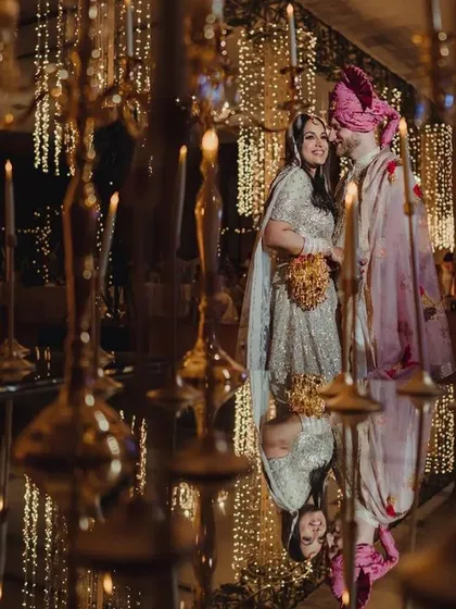 A creative shot of the couple reflected in a mirrored floor, surrounded by hundreds of candles and hanging lights. This setup creates an illusion of infinite light and romance for a reception.