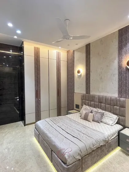 A full view of the bedroom, showcasing the padded headboard, under-bed lighting, and custom wardrobes. The wall-mounted sconces provide soft, ambient light, perfect for a relaxing evening.