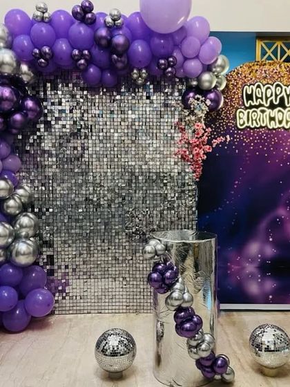 A glamorous disco-themed party with a silver shimmer wall. The purple and silver balloon arch and disco ball accents create a fun and festive party atmosphere.