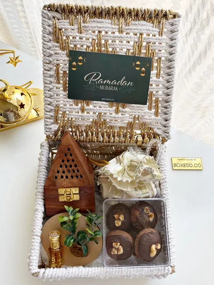 This Ramadan hamper in a woven basket includes a wooden Bakhoor burner, Attar, and chocolate-covered dates.