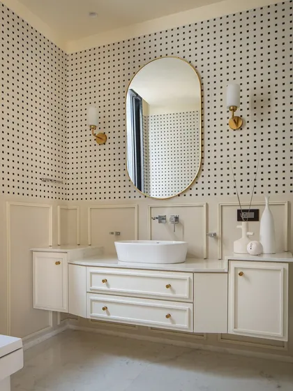 A bathroom with classic charm, featuring a custom vanity, brass fixtures, and a delicate mirror frame against a patterned wall, bringing warmth and character to this intimate space.