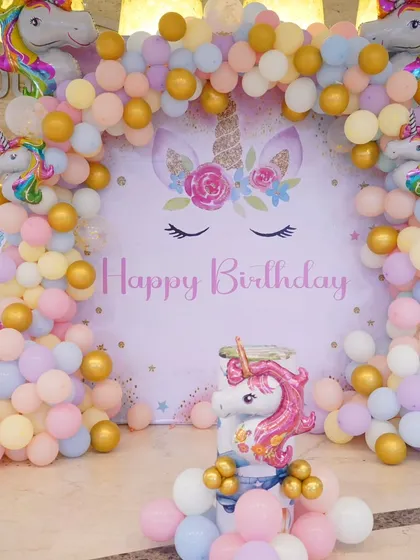 A detailed look at the Unicorn birthday backdrop, complete with a beautiful balloon arch in pastel shades and gold, and multiple unicorn figures.
