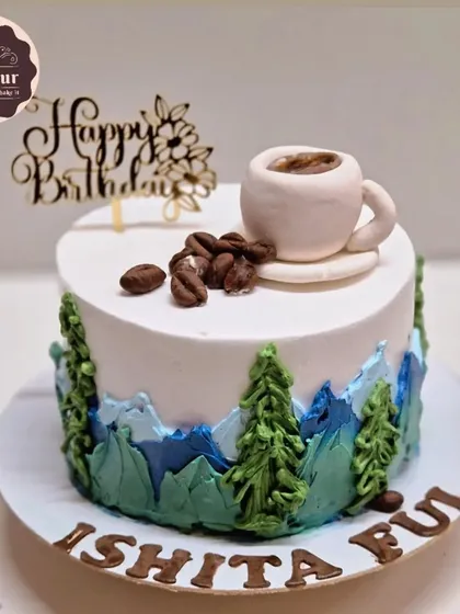 A mocha cake for someone who loves both mountains and coffee. The design features a landscape of piped-on trees and mountains with a tiny, edible coffee cup on top.