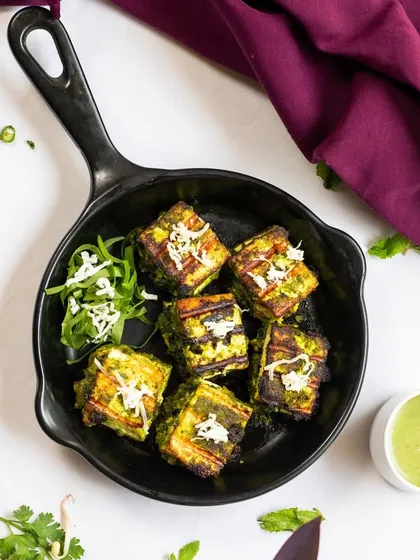 Our Hariyali Paneer Tikka, presented in a cast-iron skillet to keep it warm. The vibrant green marinade promises a fresh and herby flavor.