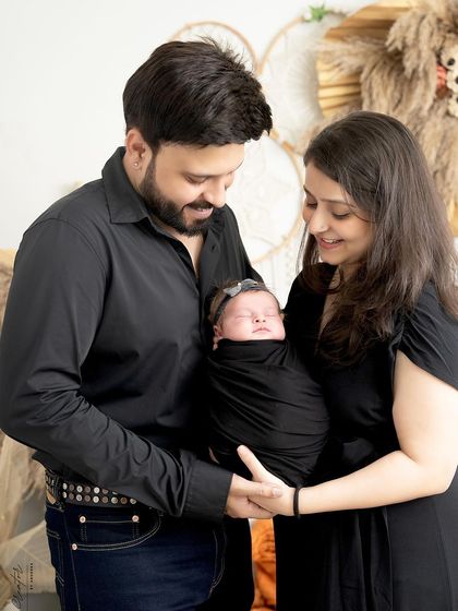 A classic portrait of new parents with their baby. The family is dressed in coordinating black outfits, creating a timeless and elegant look in our boho studio.