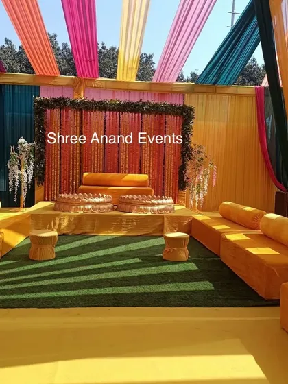 The main seating stage for a Haldi ceremony, with a backdrop of marigold strings and bright, colorful drapes.