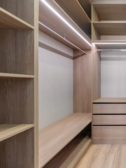 An empty walk-in closet framework made with a light oak laminate finish. This view shows the clean construction and integrated LED lighting before the clothes go in.