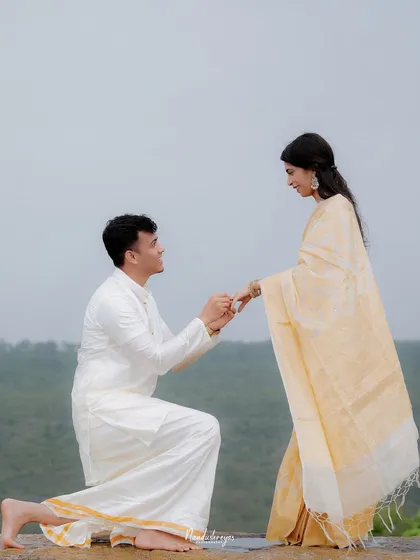 A full shot of a man proposing to his partner on a rock overlooking a green valley, a classic pre-wedding moment.