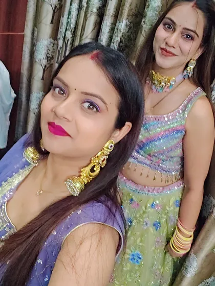 Two friends taking a selfie, one in the blue sharara and the other in a pastel sequin lehenga, ready for a celebration.