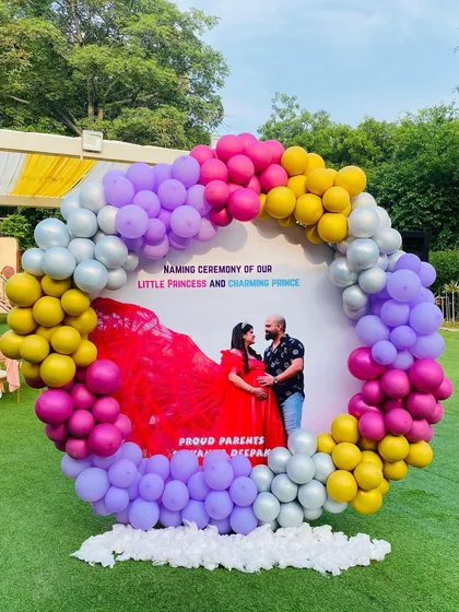 A personalized naming ceremony backdrop for a little princess and prince. The circular backdrop features a maternity photo of the parents, framed by a colorful balloon arrangement.