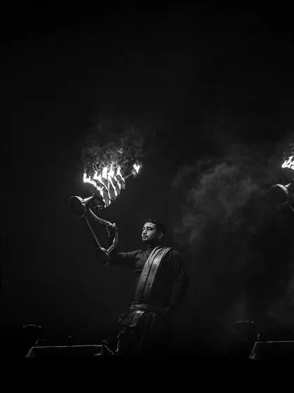 A black and white photograph of the Ganga Aarti, stripping the ceremony down to its essential elements of fire, smoke, and form. This dramatic lighting emphasizes the spiritual power of the ritual.