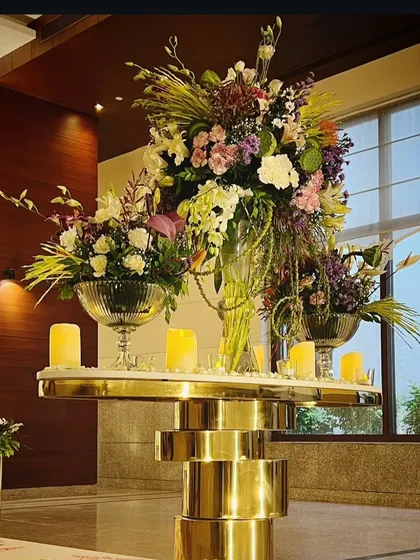 An exquisite floral arrangement in peach, purple, and ivory pastels sits atop a modern gold pedestal, welcoming guests with elegance and style.