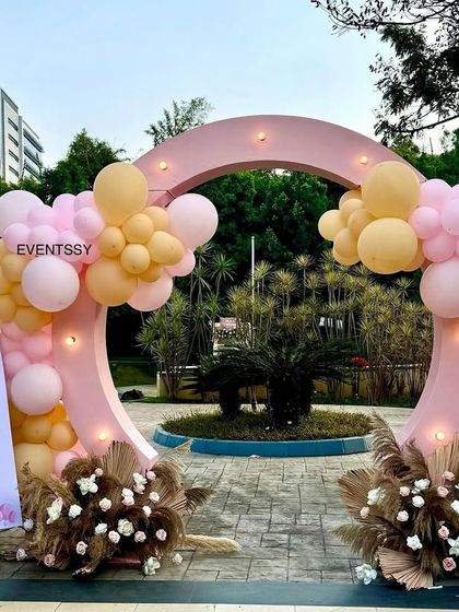 The entrance to the "Two Wild" party, featuring a circular pink arch decorated with pastel balloons and dried floral elements. A welcome sign with cute safari animals greets the guests.