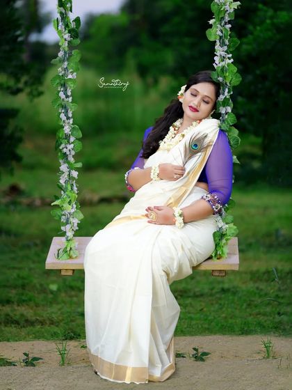 A dreamy outdoor portrait of a mother-to-be on a swing, draped in a white saree. The soft focus and natural light create a peaceful and ethereal atmosphere.