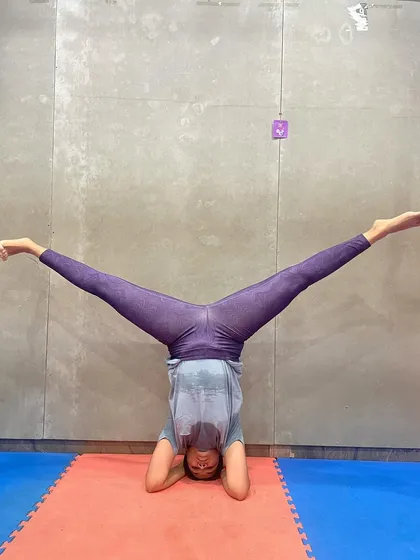 A client demonstrates a wide-leg headstand, an advanced variation that challenges flexibility and balance even further.